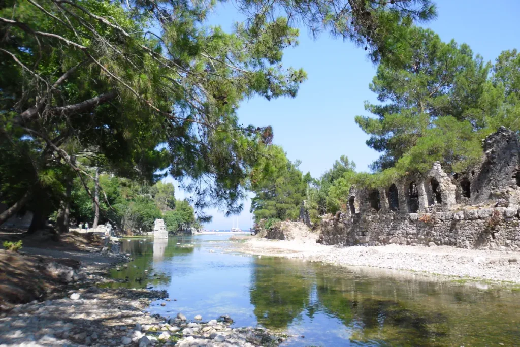 Olympos, Turkey: Where ancient Lycian ruins lie nestled within a lush forest. A tranquil river flows through the ruins, leading to a hidden beach at the edge of the Mediterranean Sea.