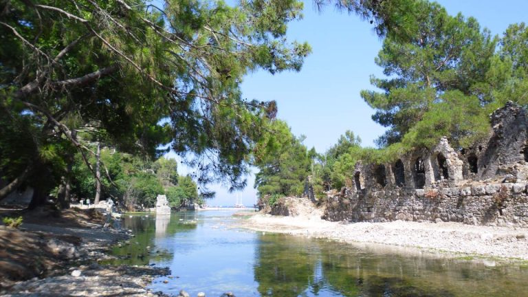 Olympos, Turkey: Where ancient Lycian ruins lie nestled within a lush forest. A tranquil river flows through the ruins, leading to a hidden beach at the edge of the Mediterranean Sea.