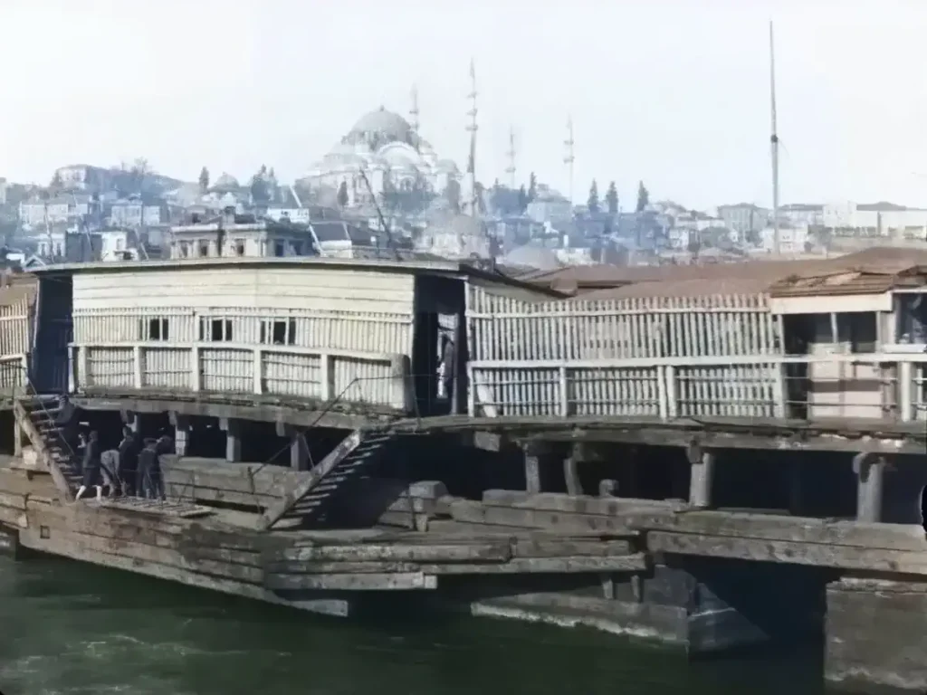 Colorized frame from the oldest video of istanbul [1897] showing the old Galata Bridge over the Golden Horn, with wooden structures, boats on the water, pedestrians on the bridge, and the Historic Peninsula with domes and minarets in the background
