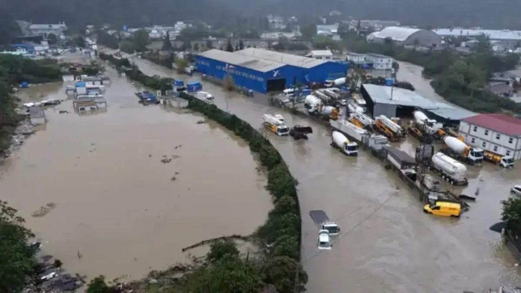 Aerial view of severe flooding in Istanbul during October 2026, showing muddy floodwaters covering an industrial area, partially submerging vehicles, and surrounding warehouses, factories, and roads.